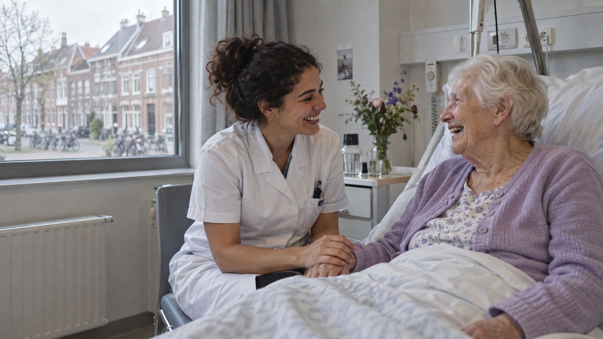 A nurse laughing with an elderly patient in a Dutch hospital room