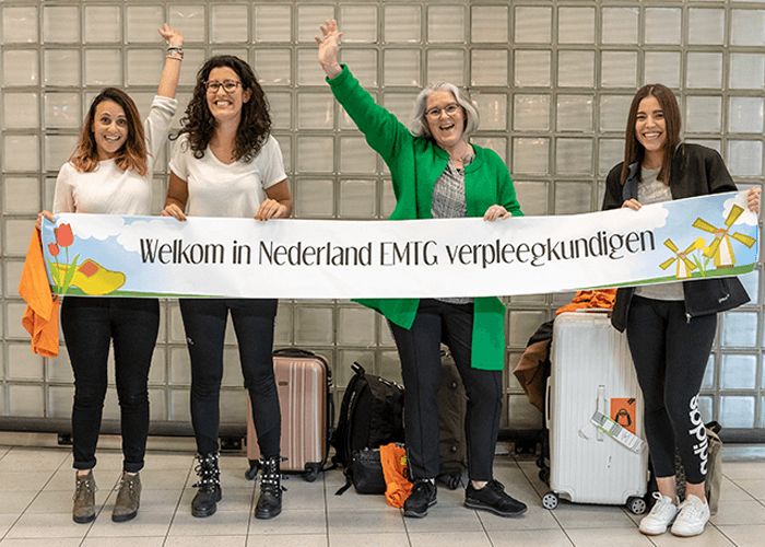 Nieuwe EMTG-verpleegkundigen worden op Schiphol verwelkomd met een spandoek 'Welkom in Nederland EMTG verpleegkundigen'